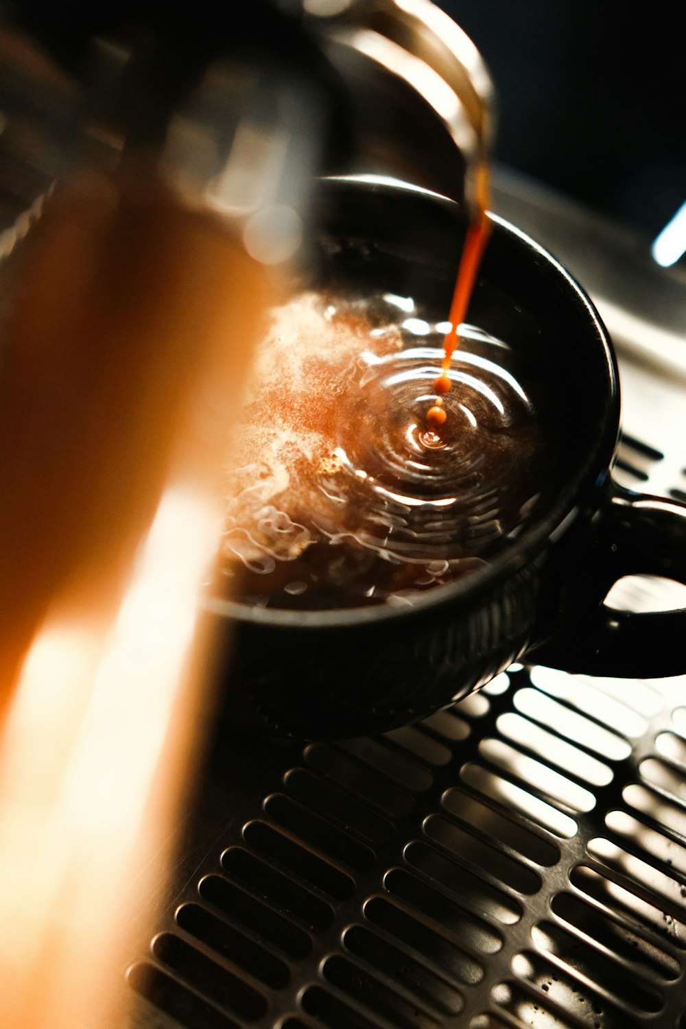 A shot of espresso pouring into a dark ceramic cup on the machine, crema rippling in the warm light