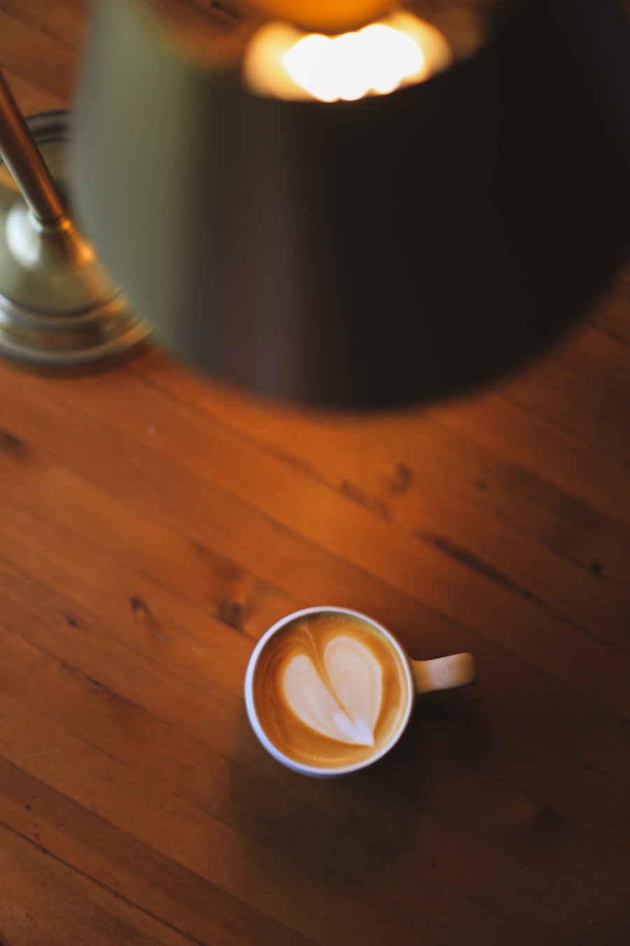 A flat white with a heart poured into the crema, on a warm wooden table under a lamp