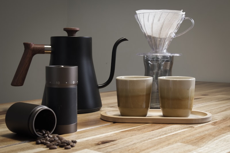 A pour-over brewer, grinder, kettle and two cups on a wooden counter