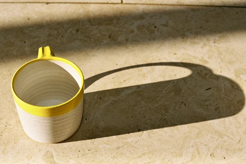 A cream stoneware mug with a yellow rim casting a long shadow