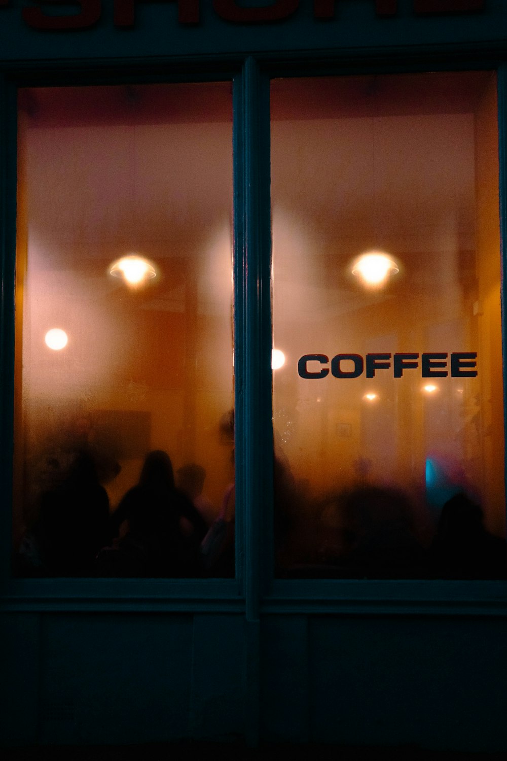 The café window at dusk, warm light and the word Coffee lettered on misted glass, people inside